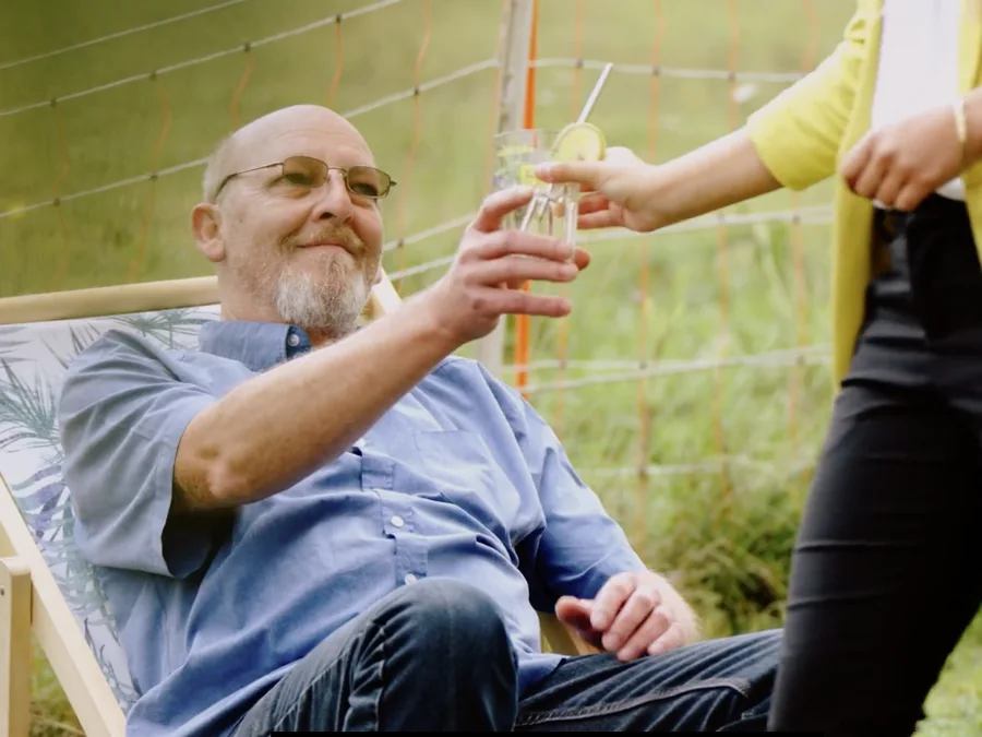 Ein Mann stößt entspannt im Liegestuhl mit einem Glas an